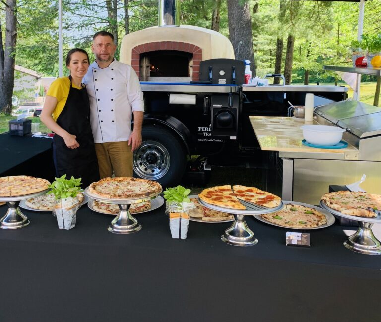 A man and a woman standing behind a table that's holing several pizzas on decorative stands