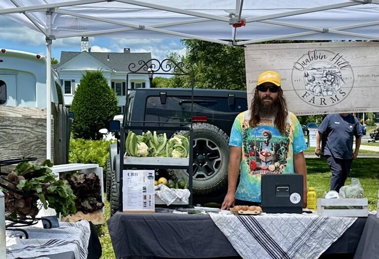 Man wearing a grateful dead tshirt standing next to table full of cauliflower, beets, and eggs